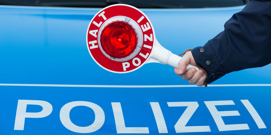 Arm der eine "HALT POLIZEI" Kelle hält mit Polizeischriftzug im Hintergrund