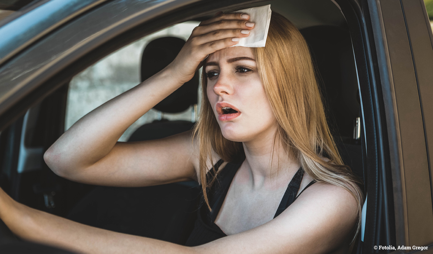 Frau schwitzt im Auto bei heißen Temperaturen