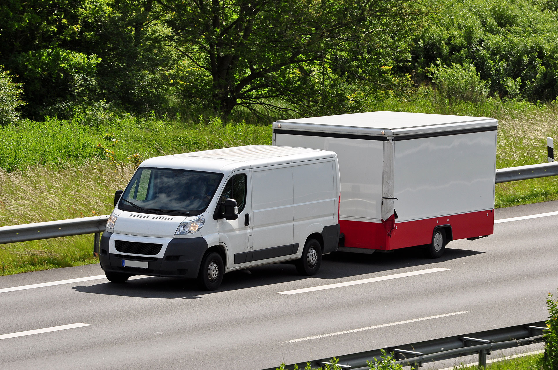 Beim Fahren mit Anhänger müssen Zuladung, Anhängelast und zulässiges Gesamtgewicht aufeinander abgestimmt sein Weißer Transporter mit geschlossenem Anhänger auf einer Straße