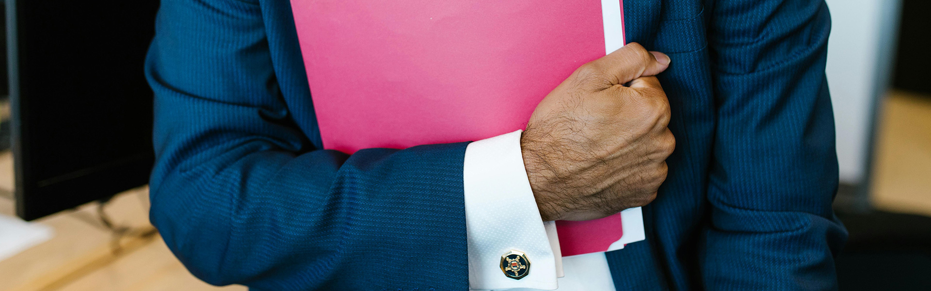 Benötigte Dokumente Ein Mann in einem dunkelblauen Anzug hält einen pinkfarbenen Ordner in der Hand.